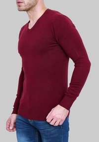 Pull en maille bordeaux avec un col en V, des manches longues et une coupe ajustée. Texture lisse, associé à un jean bleu.