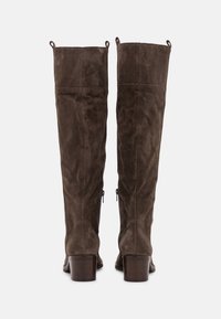 Bottes en daim marron montant au-dessus du genou, avec une texture lisse, des talons blocs et des détails de fermeture éclair sur les côtés intérieurs. Dispose d'une languette à tirer en haut.