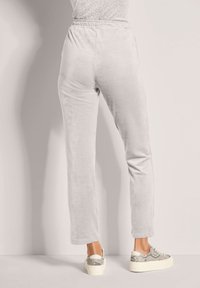 Lichtgrijze velvet joggingbroek met een elastische tailleband en rechte pijpen, gecombineerd met sneakers met een gestructureerd slangenprintje.