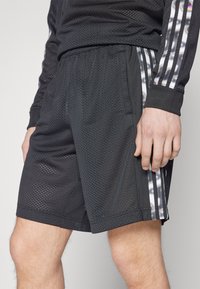 Crne mrežaste atletske kratke hlače s bočnim džepovima, s vertikalnim reflektirajućim trakama i elastičnom trakicom za udobnost i pokretljivost.