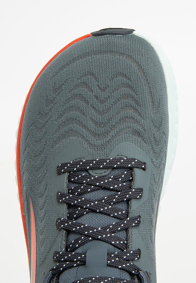 Baskets de sport avec un dessus en tricot gris, des lacets noirs avec des accents réfléchissants, et une bordure orange sur le devant ; design de semelle texturée.