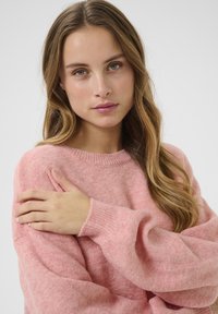 Rosa Strickpullover mit ribbed Rundhalsausschnitt, weichem Stoff und lockeren Ärmeln, präsentiert vor einem schlichten Hintergrund.