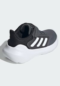 Black athletic shoe with a textured fabric upper, white three-stripe design, and a Velcro strap, featuring a cushioned white Cloudfoam sole.