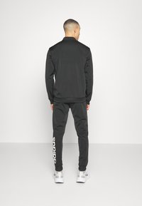 Black track jacket and joggers, featuring a smooth texture, with white 'adidas' logo on the pant leg and a fitted design.