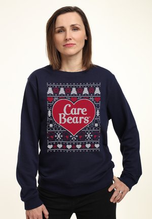 Marineblå sweatshirt med et stort rødt hjerte og teksten "Care Bears", indrammet af festlige mønstre af træer, hjerter og snemænd i hvid og grå.