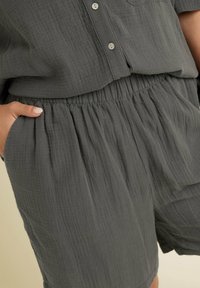 Grå, texturerad tygdräkt med elastiskt midjeband och sidofickor. Korta ärmar och en avslappnad passform. Slät knappstängning.