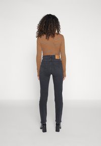 Jeans skinny a vita alta in denim grigio scuro, con una toppa sulla vita posteriore e una silhouette aderente. Maglietta a maniche lunghe a righe.
