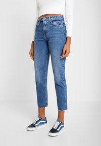 Ljusblå jeans i denim med hög midja och rå kant, kombinerat med blå och vita lågskor. Strukturerad och avslappnad design.