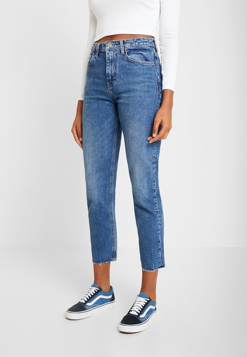 Ljusblå jeans i denim med hög midja och rå kant, kombinerat med blå och vita lågskor. Strukturerad och avslappnad design.