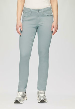 Hellblaue Skinny-Jeans mit glatter Textur, Vorder- und Hintertaschen sowie silbernem Knopfverschluss, kombiniert mit metallischen Sneakers.