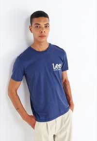 Granatowa bawełniana koszulka z okrągłym dekoltem i krótkim rękawem. Posiada białą, nadrukowaną grafikę na lewej piersi. Prosty design, luźny krój.