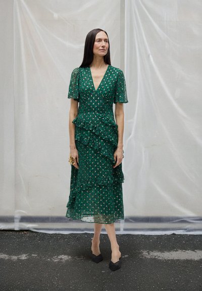 Zelené šaty s květinovým potiskem, krátkými rukávy a vrstvenými volány, s výstřihem do V. Kombinované s černými botami s špičatou špičkou.