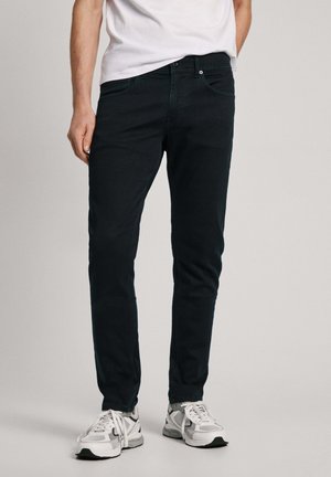 Un jean bleu foncé avec une coupe ajustée, en denim, qui présente des poches avant et une fermeture à glissière, associé à des baskets grises et blanches.