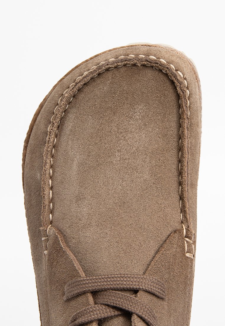 Chaussure en daim brun avec un bout rond, des coutures le long du bord et des lacets à l'avant. Texture douce et couleur atténuée.