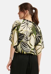 Kurzärmelige Bluse aus leichtem Stoff mit einem großen Blattmuster in Schwarz, Weiß und Grün auf einem cremefarbenen Hintergrund.