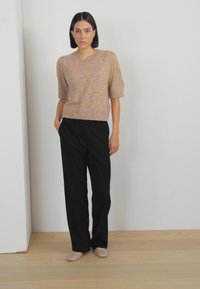 Lysebrun kortærmet sweater, løse sorte bukser og beige slip-on sko. Glat tekstur, afslappet pasform, enkelt design.