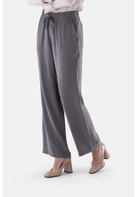 Graue, weit geschnittene Hosen aus weichem Stoff mit elastischem Bund und verstellbarem Kordelzug. Getragen mit beigen Schuhen mit Blockabsatz.