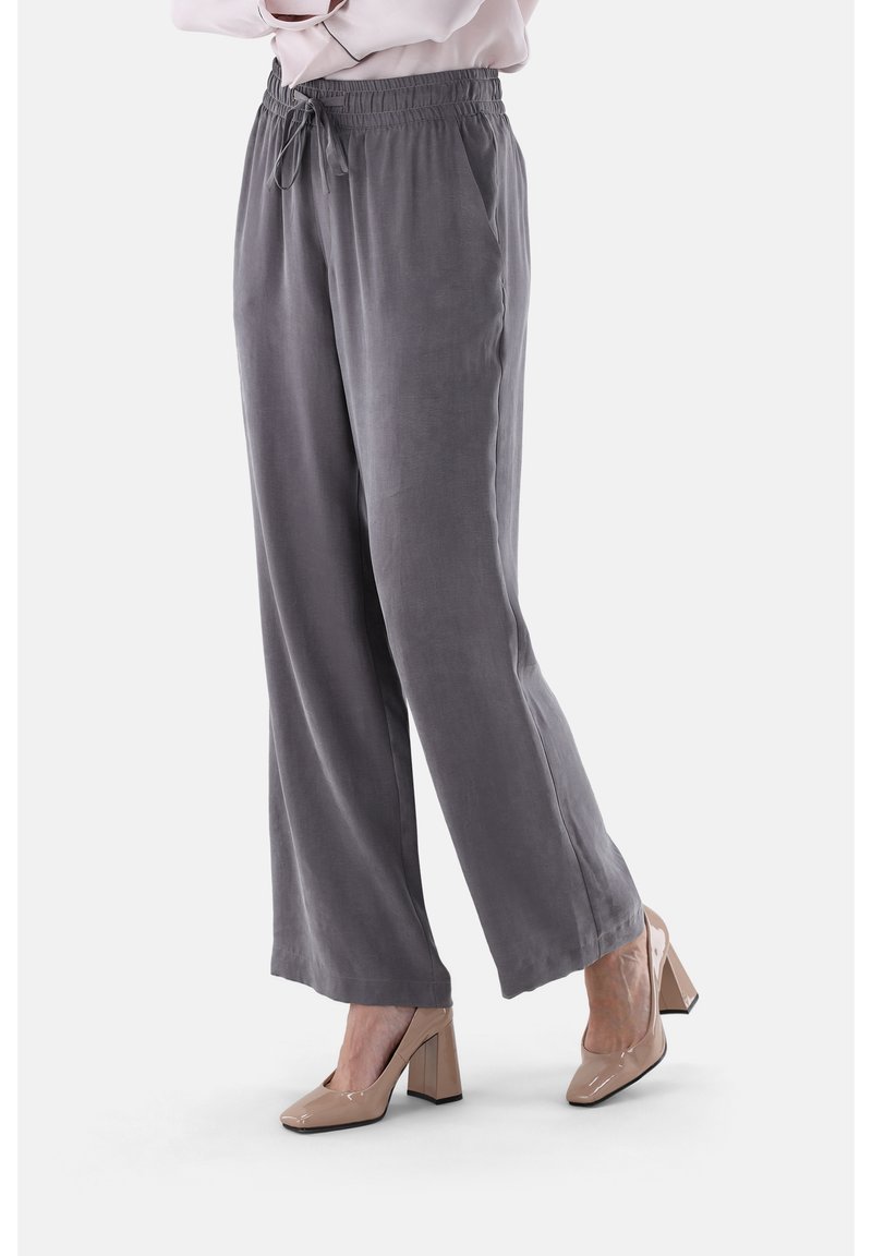 Graue, weit geschnittene Hosen aus weichem Stoff mit elastischem Bund und verstellbarem Kordelzug. Getragen mit beigen Schuhen mit Blockabsatz.