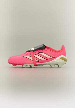 Gheată de fotbal Adidas Predator roz aprins cu dungi negre și bej, crampoane albe la talpă și o acoperire neagră a limbii pe un fundal neutru.