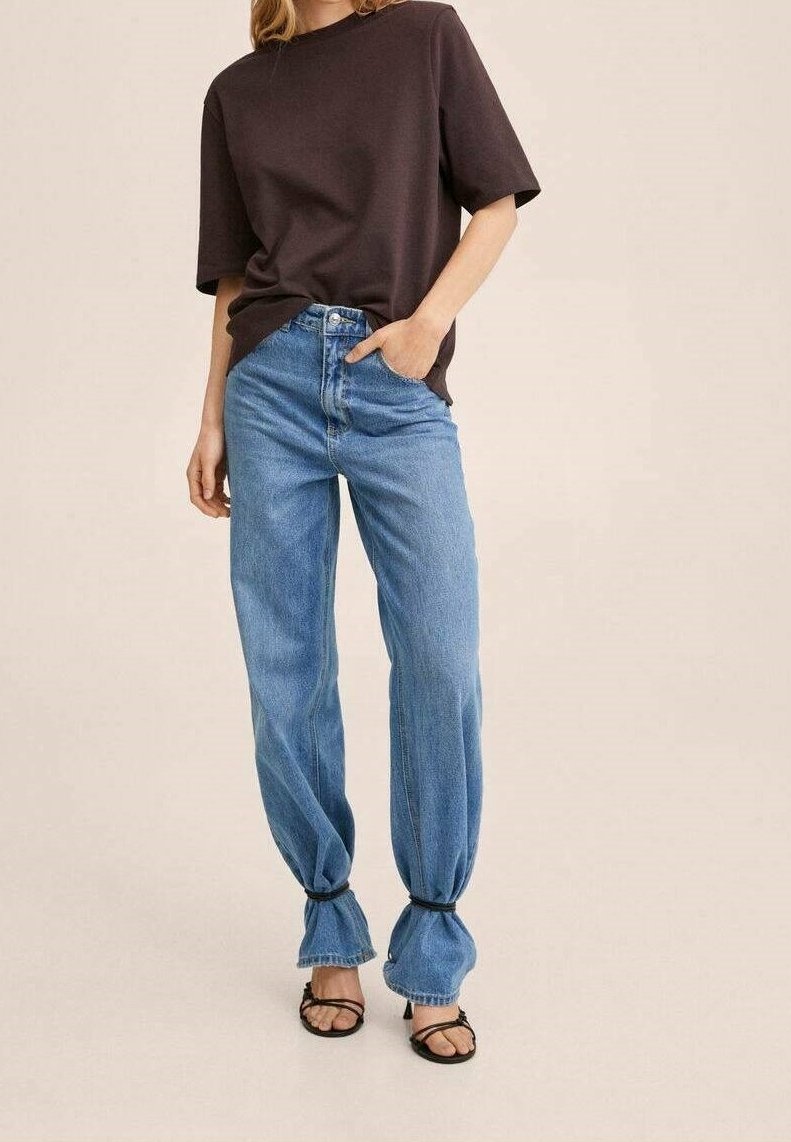 Overdimensioneret mørkebrun bomulds t-shirt parret med lyseblå denim jeans, der har en afslappet pasform og samlede manchetter ved anklerne. Sorte remsandaler.