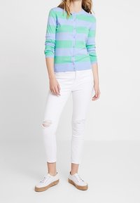 Sweter kardigan dziany w jasnoniebiesko-zielone poziome paski z guzikami z przodu. W połączeniu z białymi, podartymi jeansami typu skinny i tenisówkami.