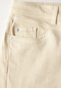 Pantalones de denim beige con un diseño de cinco bolsillos, que presentan remaches de metal, una tela texturada sutil y una cinturilla estándar.