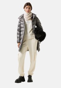 Fyldig grå dunjakke med hætte, cremefarvet sweatshirt med bjerggrafik, cremefarvet cargo-bukser og sorte chunky støvler. Sorte faux fur-detaljer.