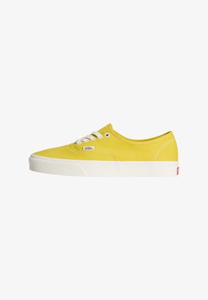 Žluté nízké plátěné tenisky Vans s bílými tkaničkami a podrážkou, zobrazující logo Vans na straně a červenou značku na patě.
