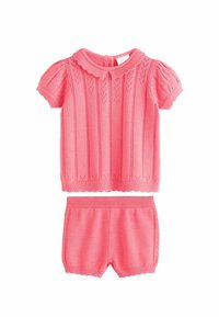 Piros, élénk színű, kötött két részes öltözet. A rövid ujjú felsőn texturált függőleges csíkok és fodros gallér található; a hozzá illő rövidnadrág bordás derékpánttal rendelkezik.