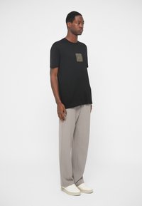 Camiseta preta de manga curta com um gráfico quadrado dourado no peito, combinada com calças largas cinza claro e ténis brancos.