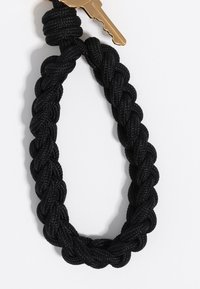 Portachiavi intrecciato nero realizzato in nylon resistente, con una chiave in metallo dorato. Il design è circolare con un anello per un facile attacco.