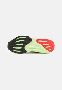 Semelle de chaussure de sport noire et verte avec un motif texturé, des accents rouges contrastants et des rainures pour la traction et la flexibilité.
