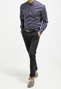 Camicia a maniche lunghe di colore viola scuro con una chiusura a bottoni, abbinata a pantaloni slim-fit neri e scarpe slip-on grigie.