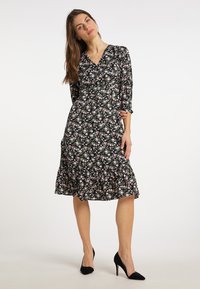 Rochie florală neagră cu decolteu în V, mâneci trei sferturi și tiv volanat. Are flori mici roz și albe pe un fundal închis.