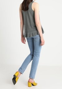 Grå ärmlös topp med utsvängd nederkant, kombinerad med ljusblå skinny jeans och gula klackskor med tjock klack och svarta detaljer.