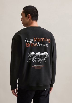 Zwart sweatshirt met een grafische print van drie mokken met gezichten en de tekst "Lazy Morning Brew Society" op de achterkant. Gezellige textuur.