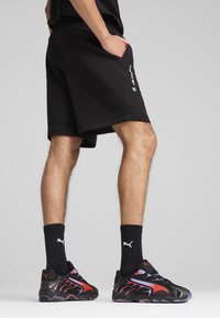 Sorte atletiske shorts med elastisk talje og sidelommer, parret med sorte sneakers med røde og lilla accenter.