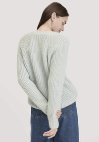 Hellblauer Strickpullover mit gerippter Textur, überschnittenen Schultern und langen Ärmeln; kombiniert mit hochgeschnittenen Denim-Jeans.