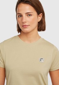 Beige t-shirt made of soft cotton, featuring a round neckline and short sleeves. Displays a circular logo patch on the chest.