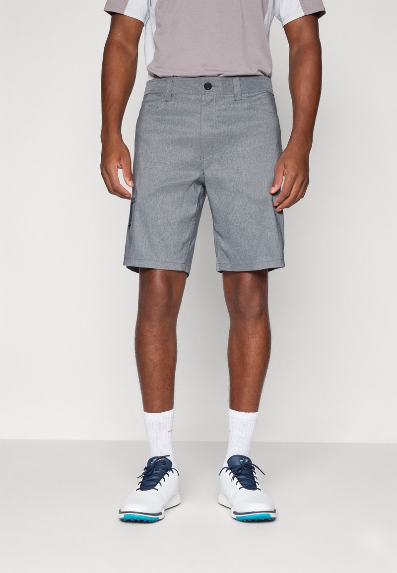 Calções cinzentos com frente plana, bolso com fecho e um corte relaxado. Combinados com uma camisa cinza claro e sapatos brancos com pormenores azuis.
