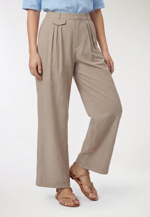 Pantaloni beige in lino a gamba larga con pieghe frontali indossati da una persona, abbinati a sandali piatti intrecciati color cuoio e una camicia azzurro chiaro.