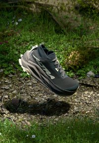 Black athletic shoe with textured upper, reflective accents, and a camp-like sole. Features tonal grey logo and laces.