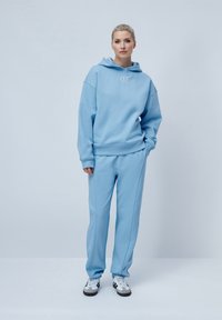 Set de hanorac și pantaloni de trening de culoare albastru deschis, realizat dintr-un material moale, cu o croială lejeră, manșete ribbed și un mic logo pe piept.