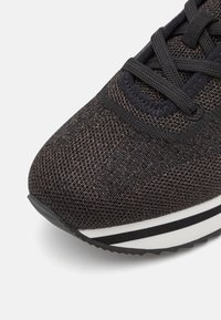 Černá a bronzová běžecká bota s texturovaným síťovaným svrškem, plochými černými tkaničkami a bíle pruhovanou mezipodrážkou, s rounded toe.