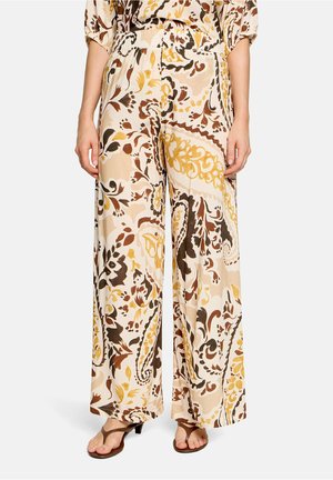 Pantalon à jambes larges avec motif floral paisley beige, marron et jaune, taille élastique, porté avec des sandales marron à talons.