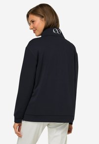 Sudadera azul marino con cuello alto, que presenta un sutil logo en el cuello, fabricada con un tejido suave y liso, con un corte relajado.