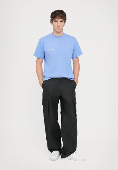 Ανοιχτό μπλε βαμβακερό t-shirt με στρογγυλή λαιμόκοψη και μικρή γραφική παράσταση στο στήθος, συνδυασμένο με φαρδιά μαύρα cargo παντελόνια και λευκά αθλητικά παπούτσια.