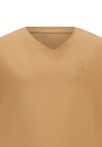 T-shirt beige a V con stoffa morbida. Presenta un logo sobrio in rilievo sul lato sinistro. Texture liscia con un design minimalista.