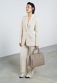 Blazer et pantalon à carreaux beige, associés à un sac à main en cuir taupe avec une poche zippée à l'avant. Des chaussures noir et blanc achèvent le look.