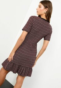 Knielanges, kurzärmeliges Kleid in Schwarz mit einem rot karierten Muster, das einen Rüschensaum und einen strukturierten Stoff aufweist.